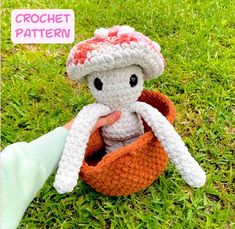 a crocheted stuffed animal in a basket on the grass with a hand holding it