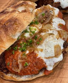 a sandwich with meat, cheese and onions on a wooden cutting board next to bread