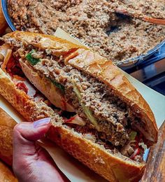 a person is holding a sandwich in front of some bread rolls and a casserole dish