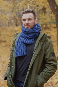 a man wearing a blue scarf standing in front of trees with leaves on the ground