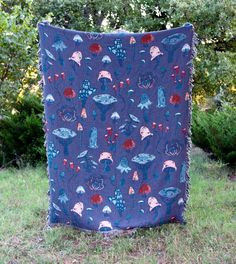 a purple blanket with blue and red designs on it sitting in the grass next to trees