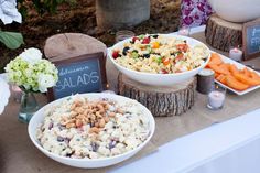 a table topped with two bowls filled with food next to plates of salad and carrots