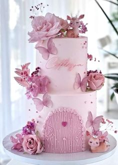 a three tiered cake with pink flowers and butterflies on the top, sitting on a table in front of a window