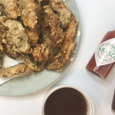 a plate full of fried food next to a cup of coffee and sauce on a table