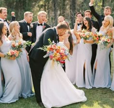 a group of people standing around each other in front of some trees and one man is kissing the woman