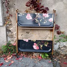 two metal trays with flowers painted on them sitting in front of a stone wall