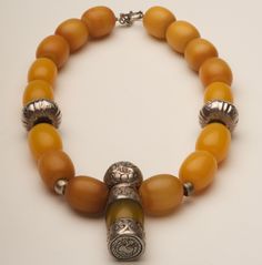 Extraordinary butterscotch copal beads enhance this very old "God" pendant.  The pendant has silver that is heavily engraved and the copal "body" contains dark markings.  Owing to the age of the pendant, there are some dents on the "head", but this does not interfere with the overall beauty or appearance of the necklace.    The melon shaped silver beads are carved as well.  The clasp is a sturdy silver toggle.  The overall length is 19 inches.  This does not include the pendant. Antique Amber Jewelry With Polished Beads, Carved Amber Amulet Jewelry, Antique Amber Jewelry With Large Beads, Traditional Amber Jewelry With Carved Details, Amber Amulet Style Beaded Necklace With Polished Beads, Amber Amulet Beaded Necklace With Polished Beads, Amber Amulet Style Jewelry With Polished Beads, Amber Amulet Style Necklace With Polished Beads, Carved Amber Spiritual Necklaces