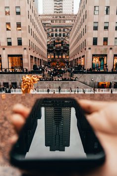 a person holding up a cell phone in the middle of a city with tall buildings