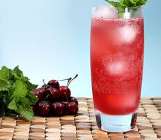 a glass filled with ice and cherries next to some minty garnish