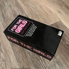 a black box with pink writing on it sitting on top of a wooden floor next to a pair of scissors