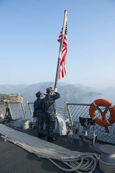 two men in uniform saluting on the deck of a ship with an american flag