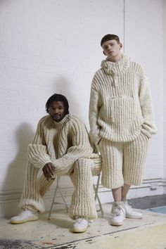 two men in knitted clothing sitting on chairs, one with his legs crossed and the other wearing white sneakers