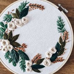 a white embroidery hoop with flowers and leaves around it on a wooden table next to a pair of scissors