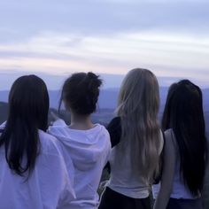 three girls standing on top of a hill looking at the sky