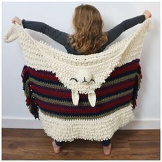 a woman standing in front of a white wall wearing a crocheted shawl