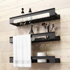 two black shelves with white towels and other bathroom items on them in front of a wooden wall