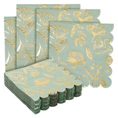 four napkins with gold foil flowers on blue and green paper, each folded in different sizes