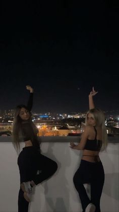 two women standing next to each other in front of a cityscape at night