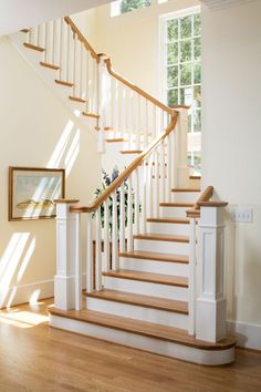 a white staircase with wooden handrails next to a framed painting on the wall