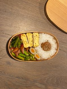 a wooden plate filled with rice, meat and veggies on top of a table