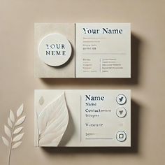 two white business cards sitting on top of each other next to a plant with leaves