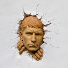 a clay face is shown in the middle of a cracked up wall with hands on it