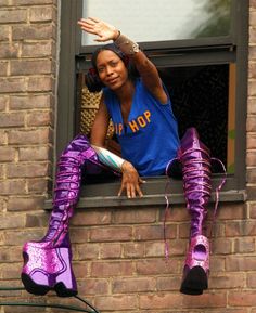 a woman sitting on the window sill waving at someone in her purple booties