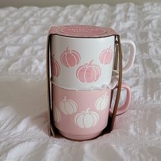 a pink and white coffee cup with pumpkins on it sitting on top of a bed