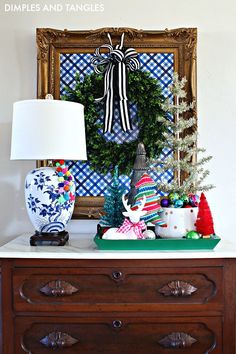 a christmas wreath on top of a dresser next to a lamp and painting with plaid