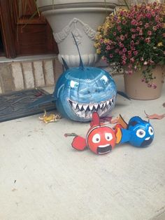 two toy fish sitting on the ground next to a potted plant