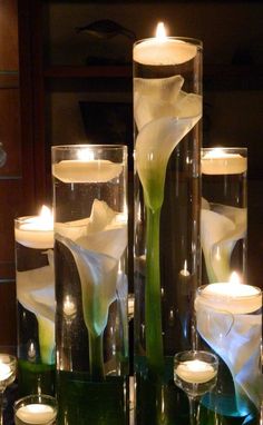 candles are lit in glass vases with flowers and leaves on the bottom one is filled with water