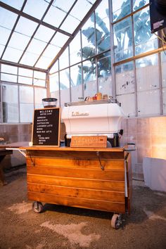 a coffee machine sitting on top of a wooden cart next to a table with a sign