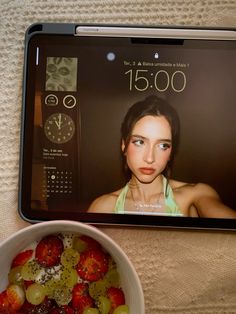 a bowl of fruit next to a tablet with the face of a woman on it