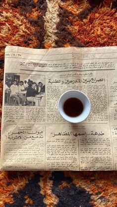 a cup of coffee sitting on top of a newspaper with some writing in arabic and english