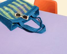 a blue bag sitting on top of a purple table next to a pair of sunglasses