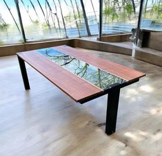 a wooden table with glass top sitting in front of large windows on the side of a building