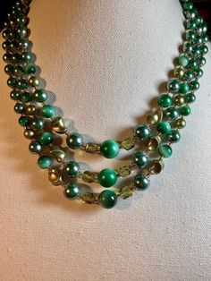 Attractive vintage lucite and glass Japanese 3 strand bib necklace. Large green lucite bead from 13mm down to 7mm round with similar size twisted beads. The addition of 8mm transparent green faceted glass beads and glass seed bead spacers really clinches the elegant look. The complete shortest length with 3 inch adjustable extension is 19 inches. Stamped Japan on the silver tone clasp. Good condition with little wear and a hook clasp. (B484) Green Multi-strand Beads For Jewelry Making, Multi-strand Green Large Beads, Green Double Strand Beaded Necklace, Green Round Beads Costume Jewelry, Green Multi-strand Costume Jewelry, Multi-strand Green Faceted Beads, Green Multi-strand Polished Beaded Necklace, Adjustable Green Double Strand Necklace, Vintage Green Double Strand Necklaces