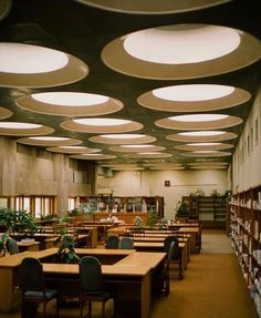 an empty library filled with lots of tables and chairs next to bookshelves covered in plants