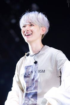 a young man with white hair smiles at the camera while wearing a t - shirt