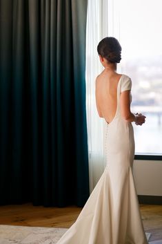 a woman standing in front of a window wearing a wedding dress