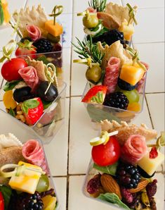 four plastic containers filled with assorted fruits and veggies on top of a white tile floor