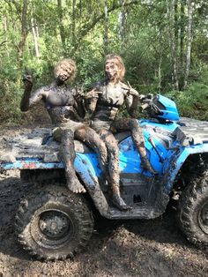 two people riding on the back of a blue four - wheeler in mud covered forest