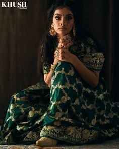 a woman sitting on the ground in a green and gold dress with her hands clasped