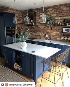 a kitchen with blue cabinets and an island in front of a brick wall that has potted plants on it