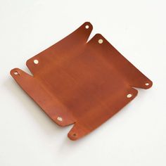 two pieces of brown leather sitting on top of a white surface with holes in the middle