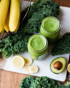 two mason jars filled with green smoothie next to sliced avocado and bananas