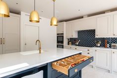 an open drawer in the middle of a large kitchen island with marble countertops and gold pendant lights