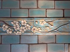 a tile wall with flowers and vines on the bottom, painted in metallic blue tint