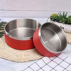 two red and silver bowls sitting on top of a table next to succulent plants