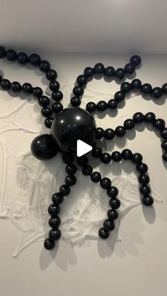 a spider made out of black beads on top of a white surface with an arrow in the middle